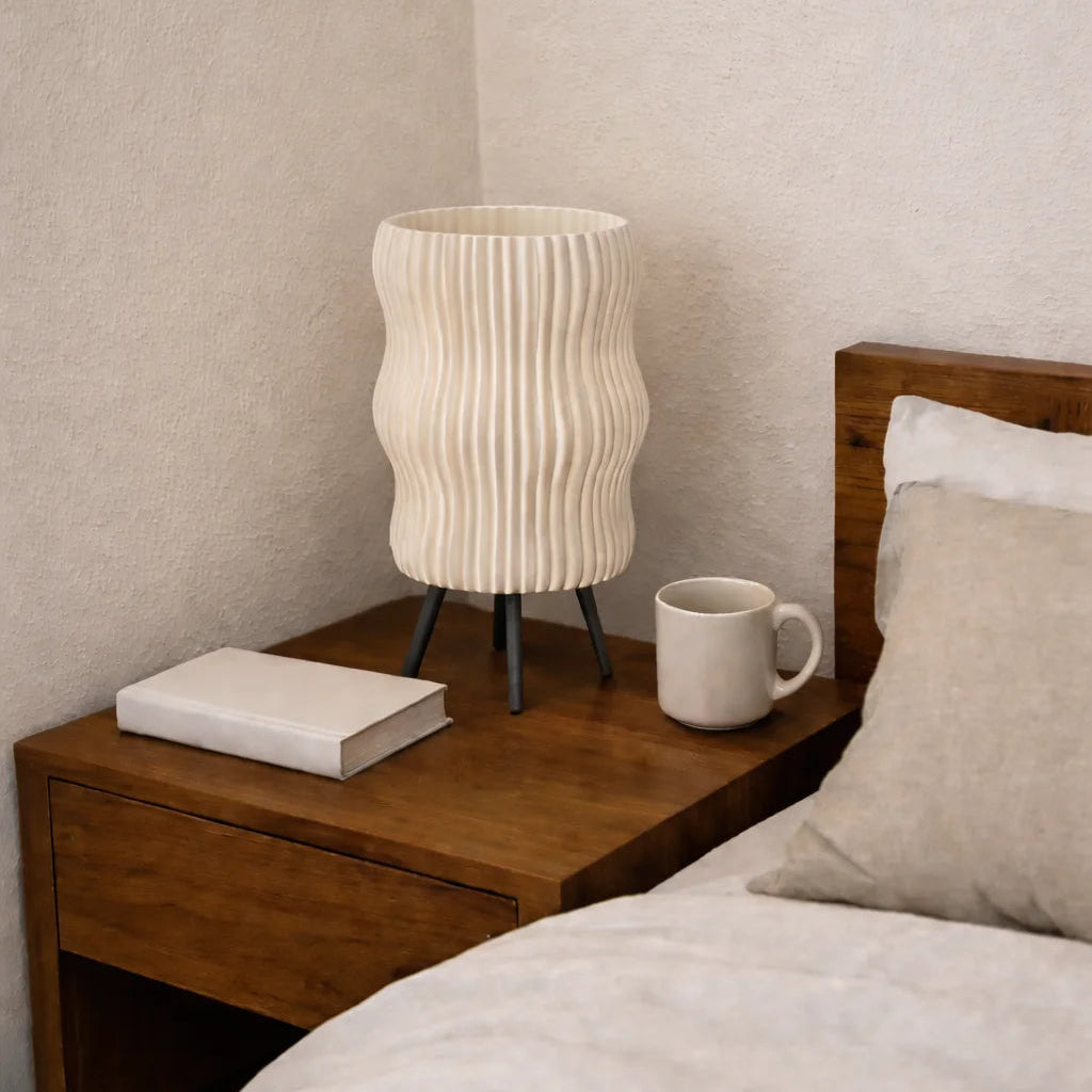 Wooden nightstand with a lamp, book, and mug next to a bed with pillows.