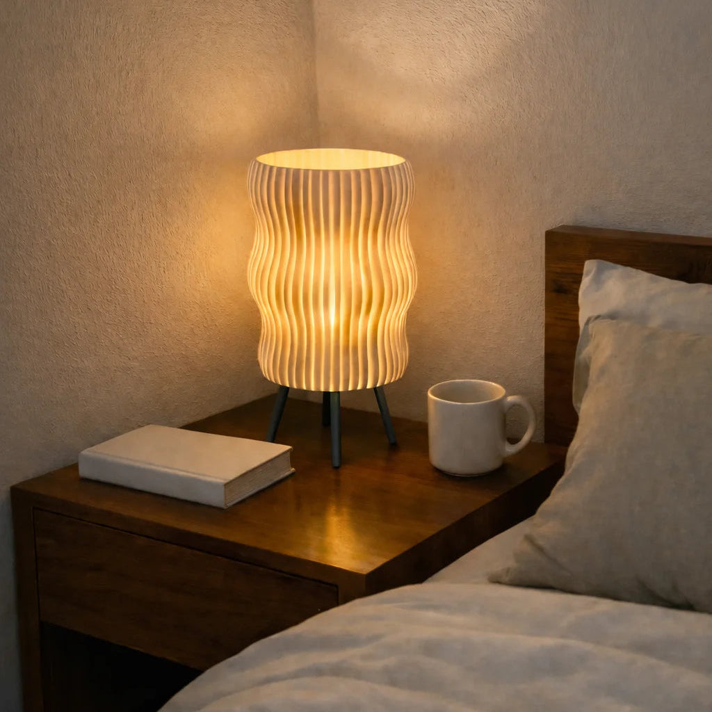 Lamp on a bedside table next to a bed with a book and mug.